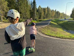 Foto. Två barn med sparkcyklar på en gång- och cykelväg.