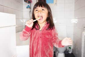 Flicka i röd tröja borstar tänderna.