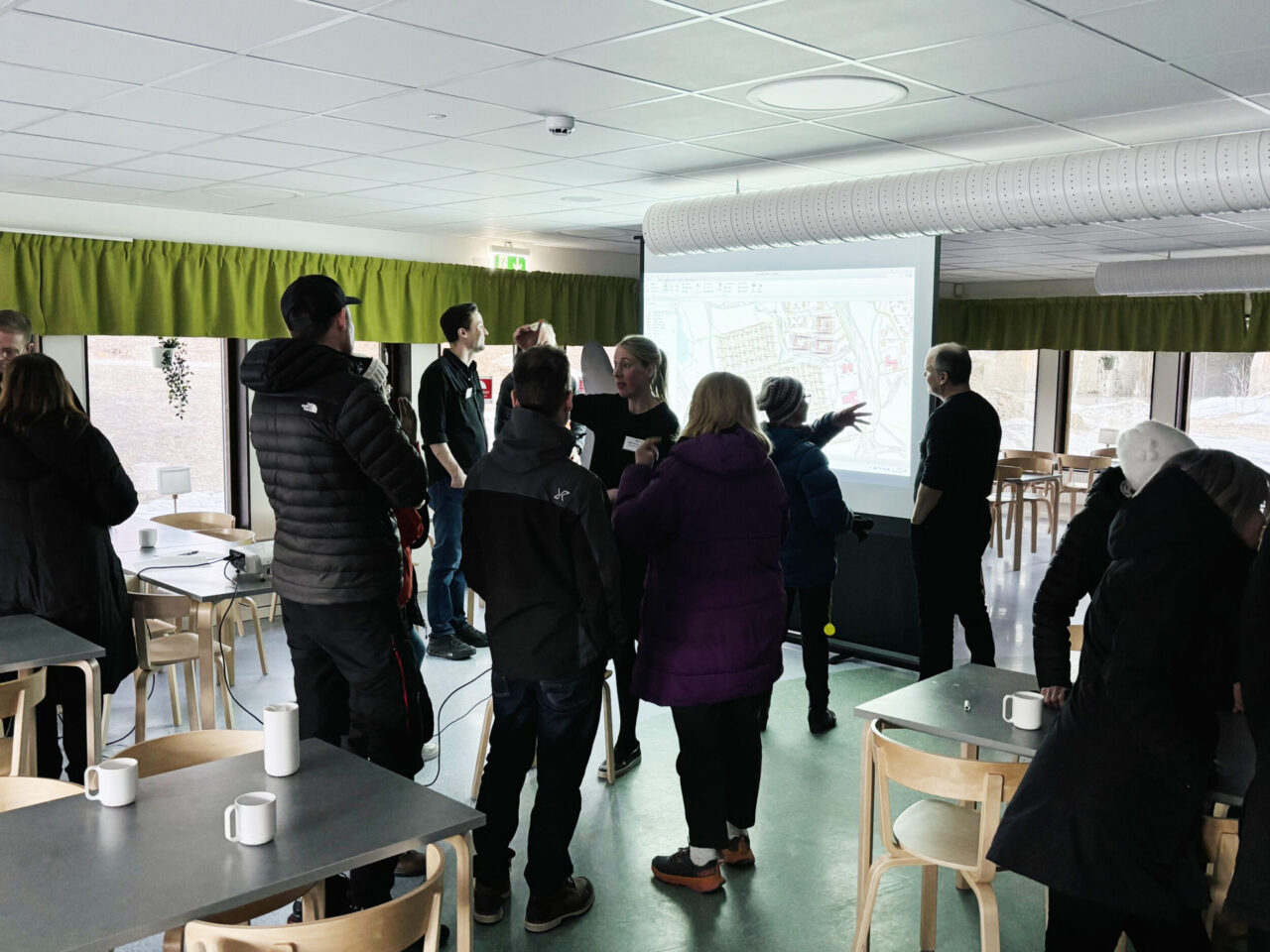 Fotografi. Deltagare och representanter från Lumire och Luleå kommun står och diskuterar framför en projektorduk som visar en kartbild.