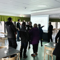 Fotografi. Deltagare och representanter från Lumire och Luleå kommun står och diskuterar framför en projektorduk som visar en kartbild.